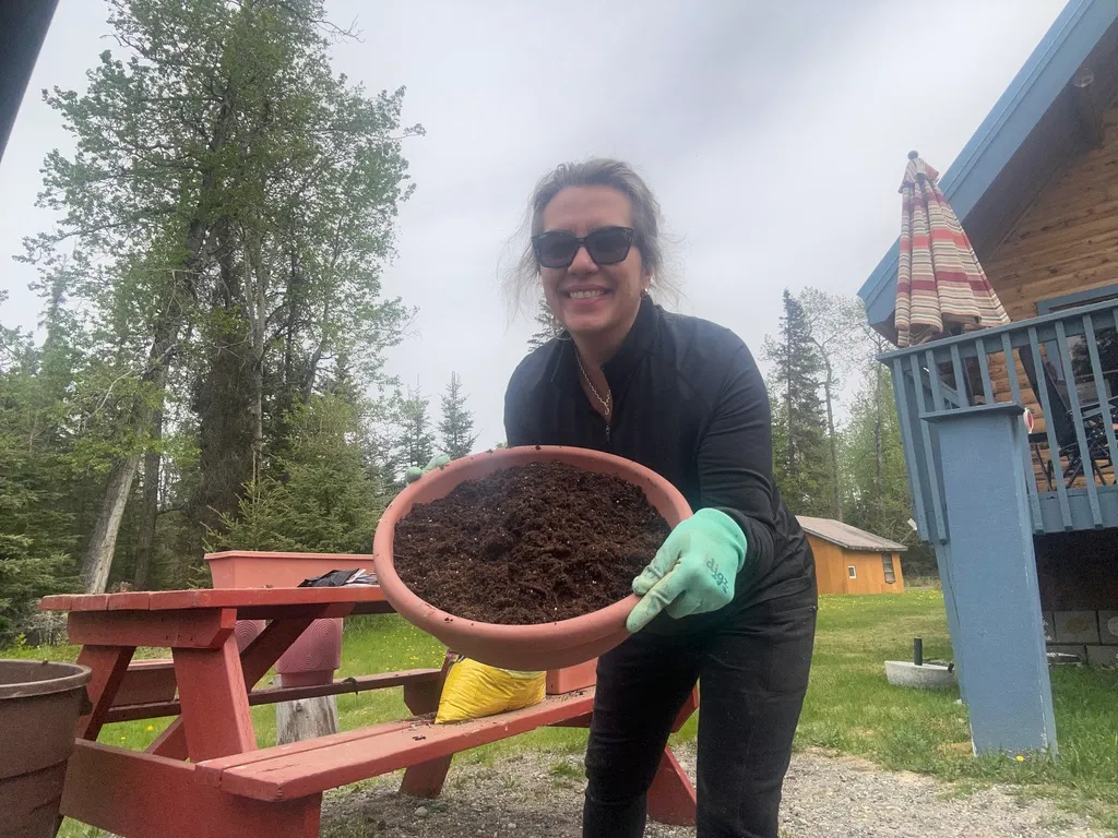 Me holding up a freshly filled pot of soil in front of the cabin